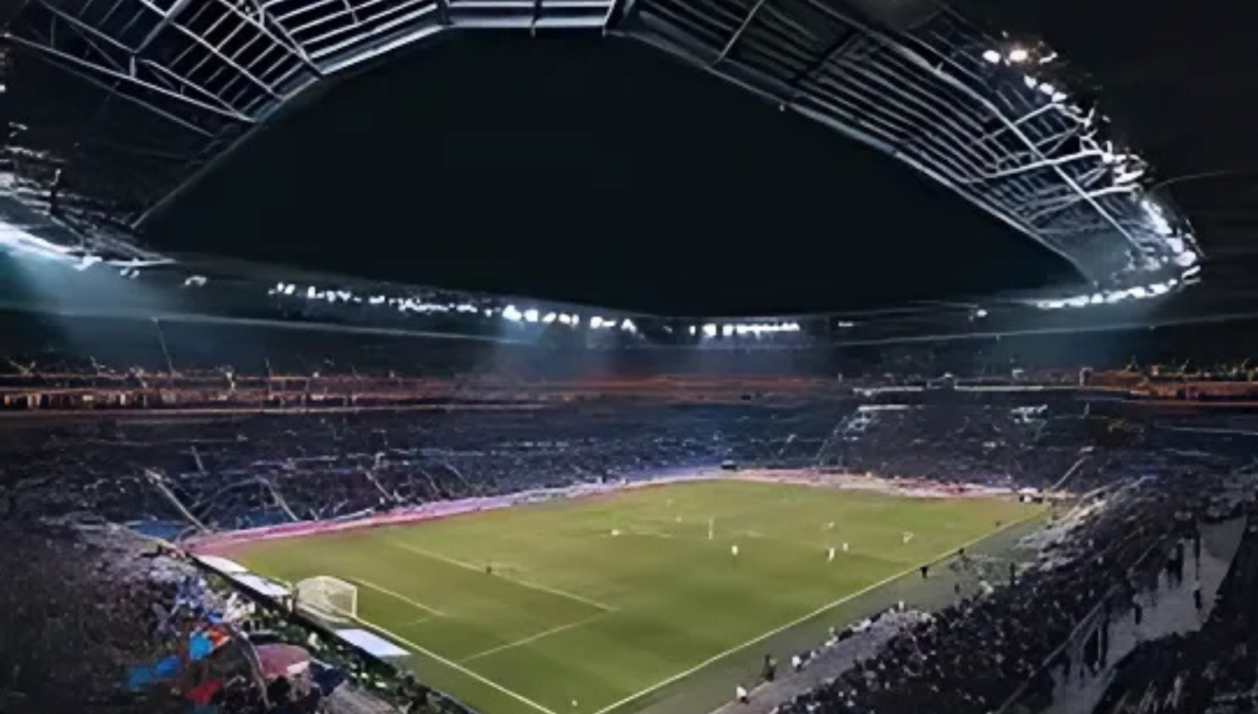 Gambar stadion sepak bola pada malam hari dengan pencahayaan penuh menjelang pertandingan.