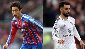 Dua pemain sepak bola, satu berseragam merah-biru dan satu lagi berseragam putih, berdiri berdekatan di lapangan.